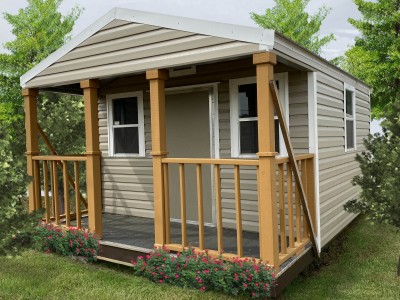 Lofted portable cabin with porch, featuring wooden railing and flower beds, set in a grassy area among trees, showcasing storage solution options.