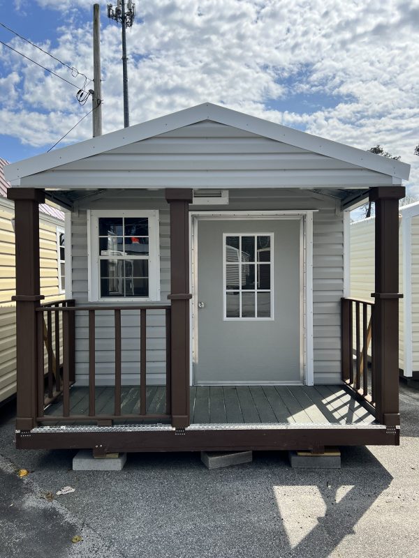 10×4-Deck-with-Railing-600×800 Portable storage building with a gray exterior, front door, and wooden railing, showcasing customizable design options for sheds at Repo Lot.