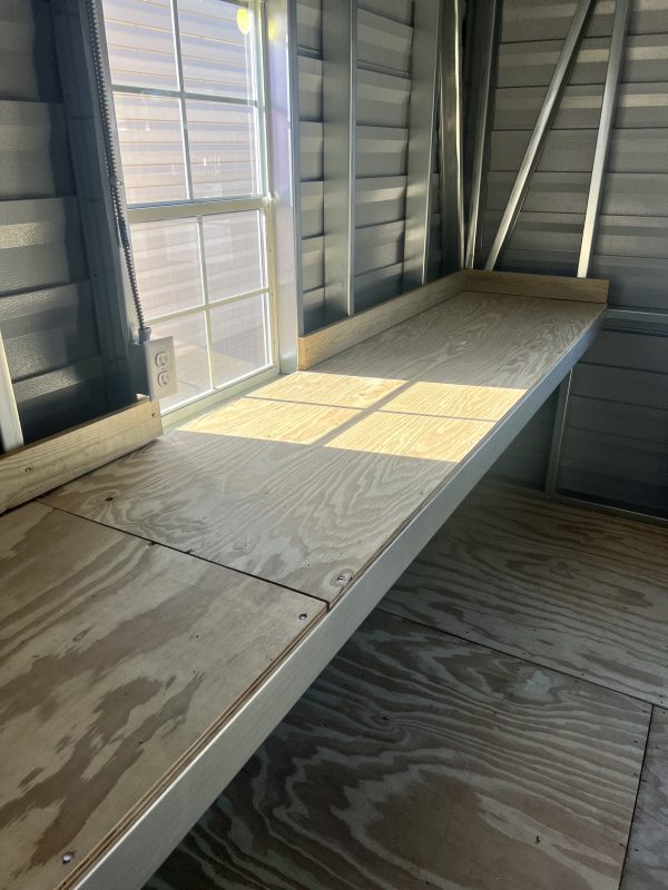 24-Shelving-600×800 Interior view of a portable storage building featuring a wooden shelf, window allowing natural light, and metal framing, highlighting customizable storage solutions by Repo Lot.