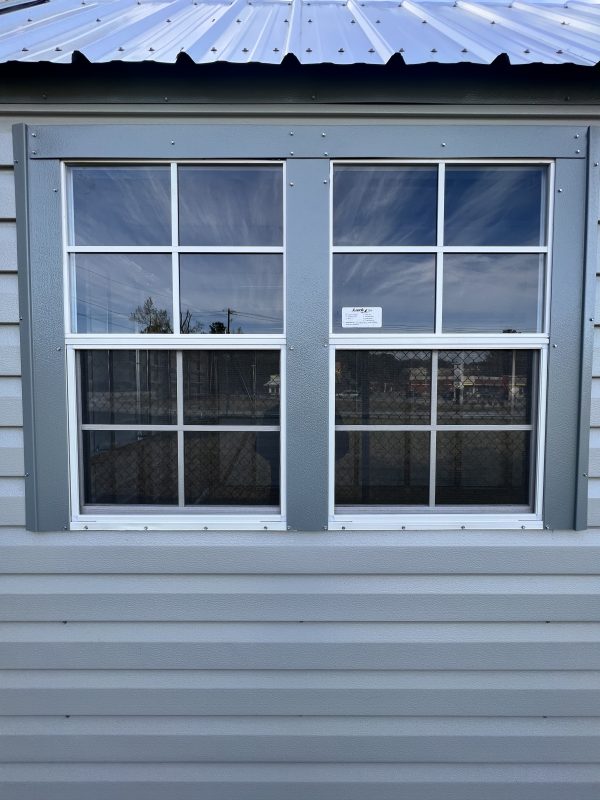 30×40-Extra-Large-Window-600×800 Gray window with four panes and a label, set on a portable building with horizontal siding and a metal roof, showcasing customizable features for portable storage solutions.