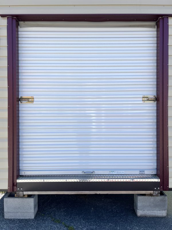 6×6-Rollup-Door-600×800 Portable storage building with a roll-up door, featuring white metal slats and bronze accents, positioned on concrete blocks, showcasing customizable storage solutions by Repo Lot.