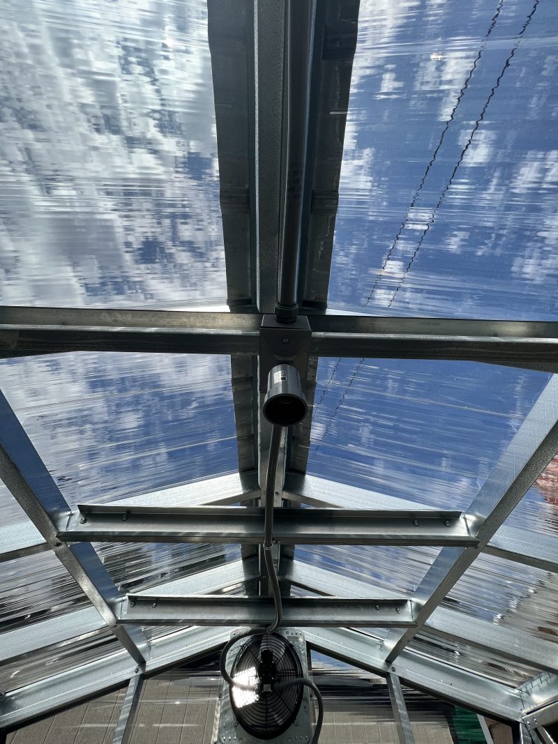 Photo-Mar-22-3-03-47-PM-800×1067 Interior view of a portable storage building showcasing metal framework, translucent roofing, and a ventilation fan, highlighting customizable features for storage solutions.