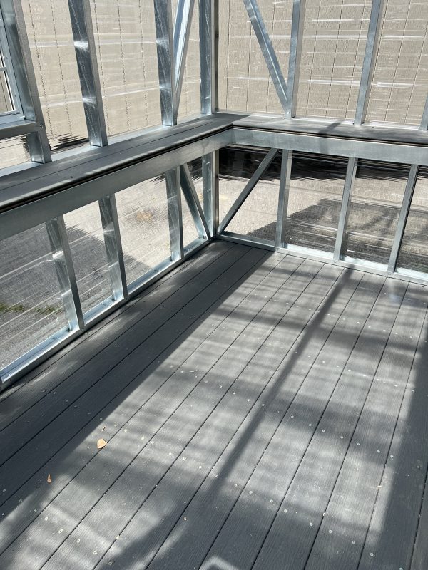 Plastic-Composite-Flooring-and-Shelving-in-Greenhouse-600×800 Interior view of a greenhouse featuring composite flooring, metal framing, and ample natural light, relevant to customizable portable storage solutions offered by Repo Lot.