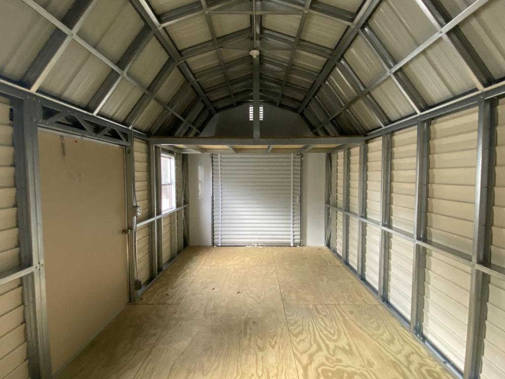 Interior view of a lofted mini garage featuring a gambrel roof, wooden flooring, and metal framing, showcasing ample storage space for seasonal items and equipment.