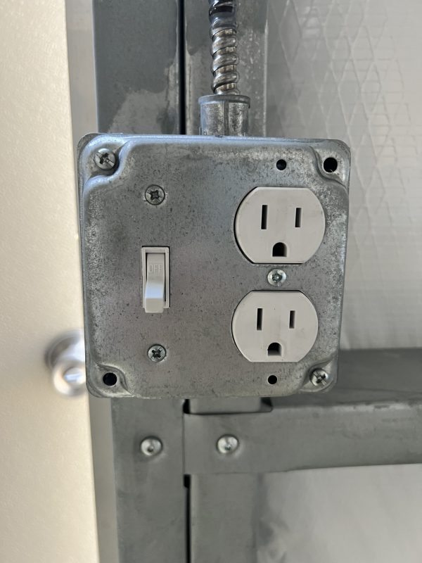 Standard-Light-Switch-Outlet-600×800 Standard electrical outlet with switch, mounted on portable storage building interior, showcasing customization options for electrical features.
